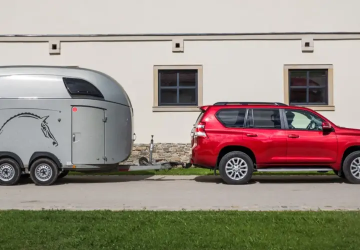 Czerwony SUV ciągnie przyczepę z wizerunkiem konia.